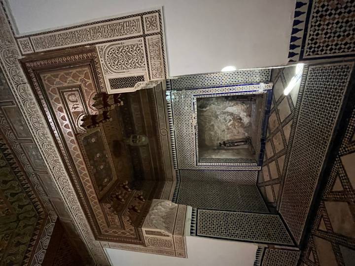 Dimly lit decorated chamber with intricate zellij tilework and carved ceiling inside a Moroccan palace.
