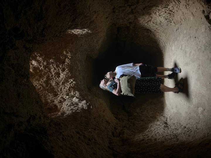 Woman and child gaze up at light streaming through an opening in a rugged cave interior.