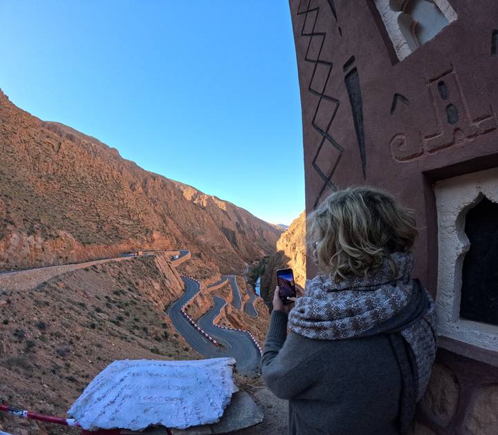 Traveler photographs a serpentine mountain road from a cliffside viewpoint.