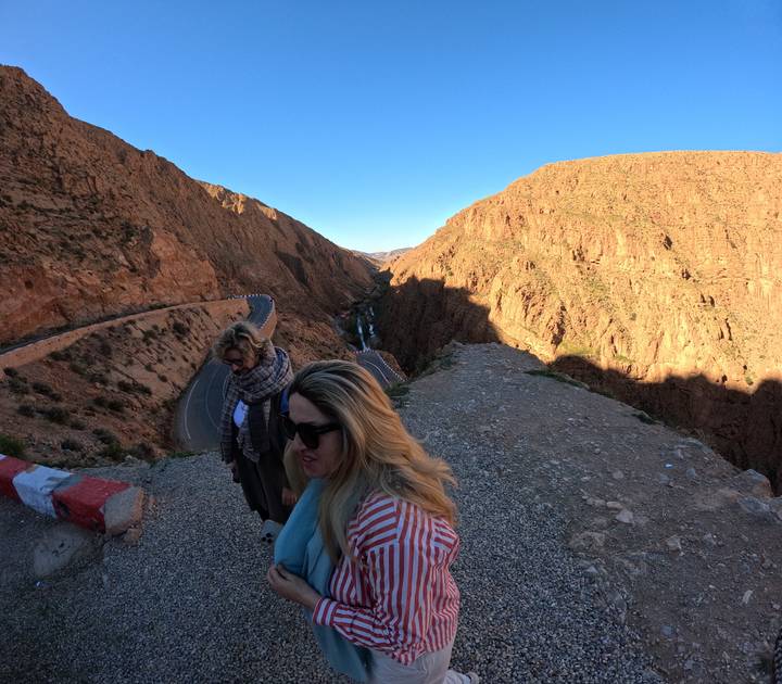 Two women stand at a cliff edge overlooking a deep gorge bathed in late-day light.