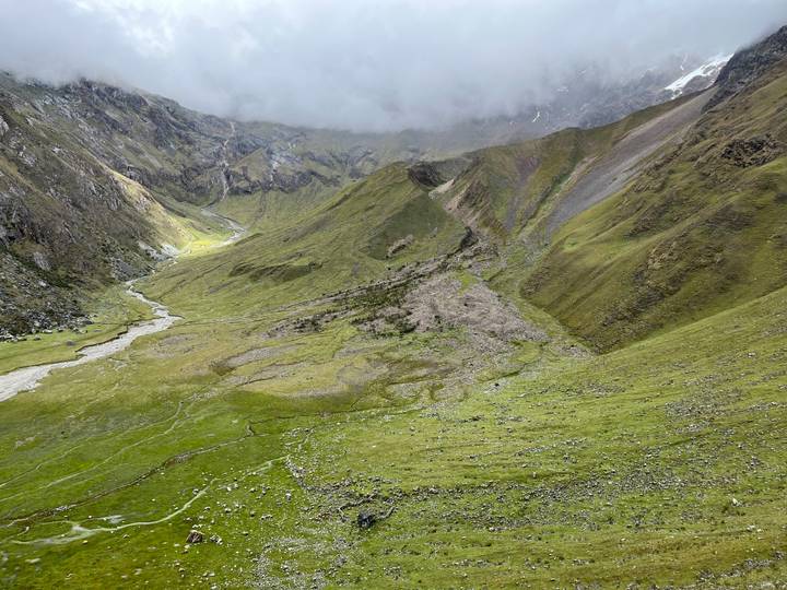 High-altitude green valley and meandering stream under swirling mountain mist on the Salkantay trek.