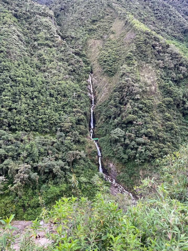Tall slender waterfall cuts through dense green jungle hillside in Peru.