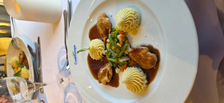 Elegant main dish of poultry with piped mashed potatoes and vegetables in rich sauce.