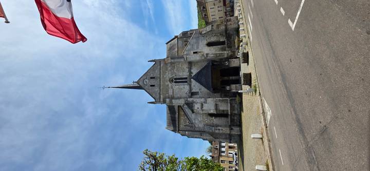 Stone church with tall spire in small town square beneath blue sky and flag.