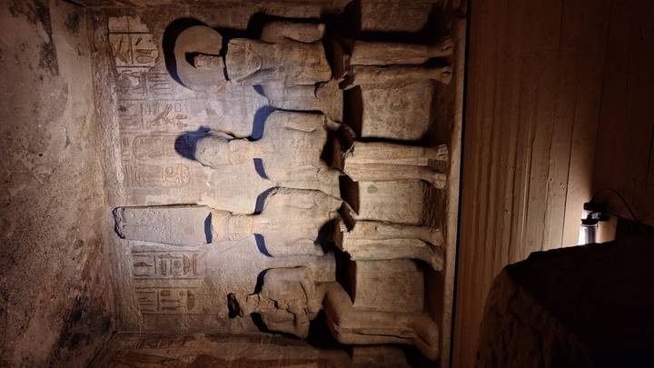 Dim chamber with four seated sandstone statues illuminated by a spotlight in Abu Simbel’s interior.