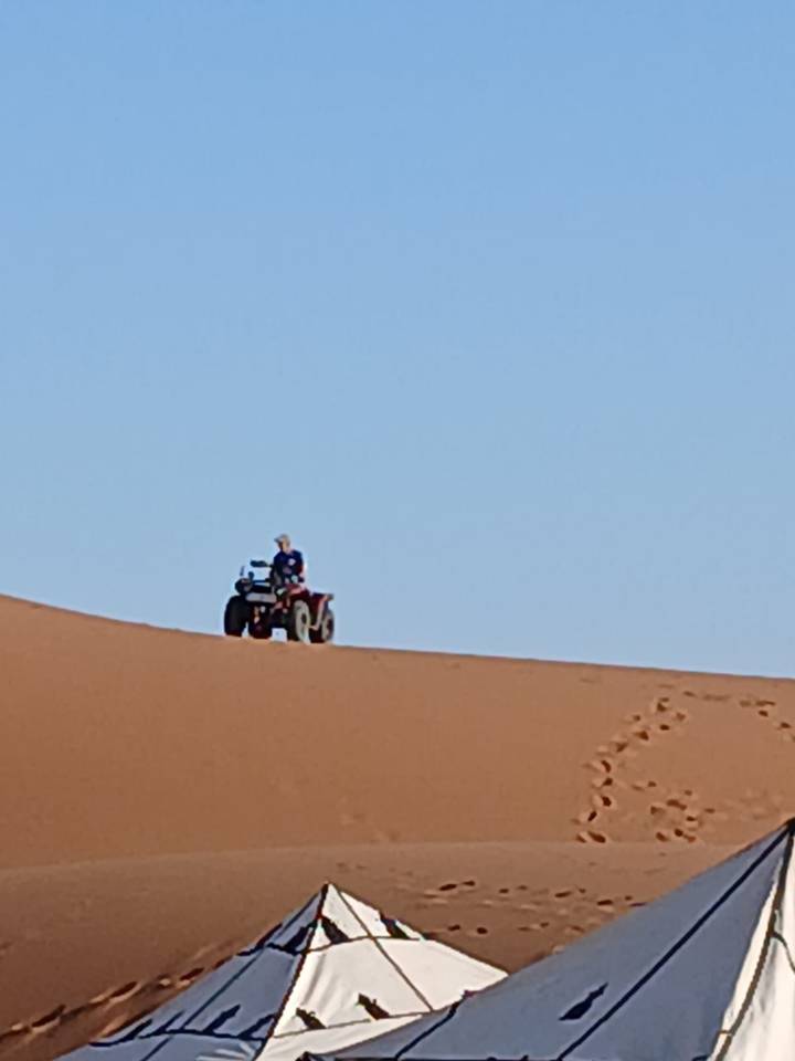 Blurry distant shot of a person riding a quad bike on top of a sand dune.