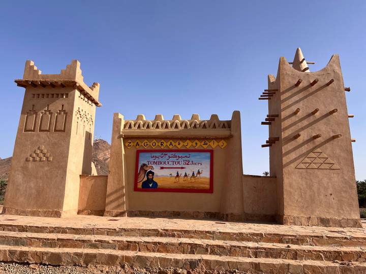 Clay-colored desert gateway monument in Zagora with sign pointing to Timbuktu