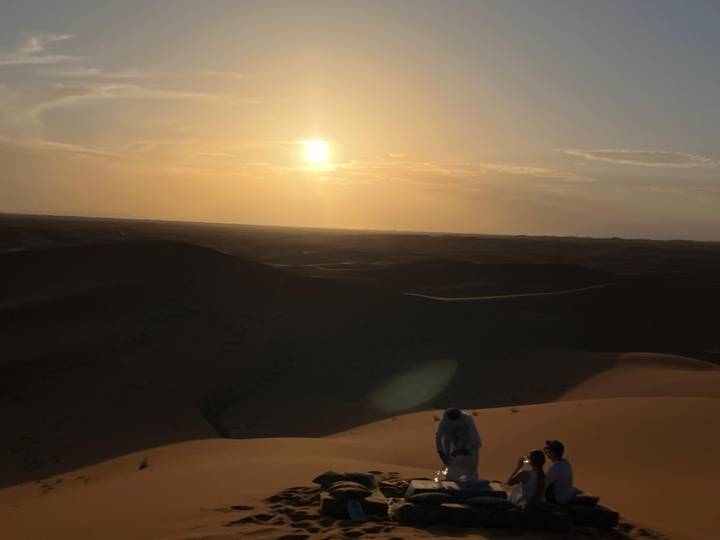 Low-light view of tiny figures on high dune with hazy sun setting over dark sands