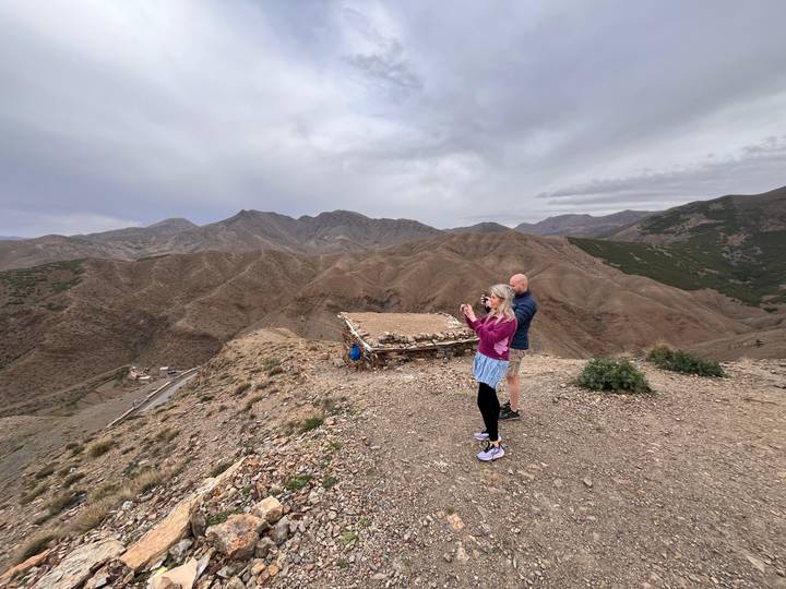 Two travelers photographing rugged Atlas mountain landscape from windy viewpoint