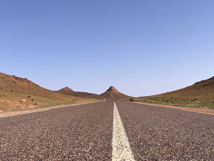 Straight desert highway leading to cone-shaped hill under cloudless blue sky
