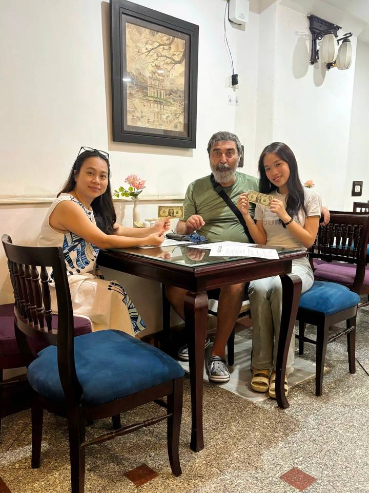Three people sitting at a café table holding US dollars while smiling at the camera.