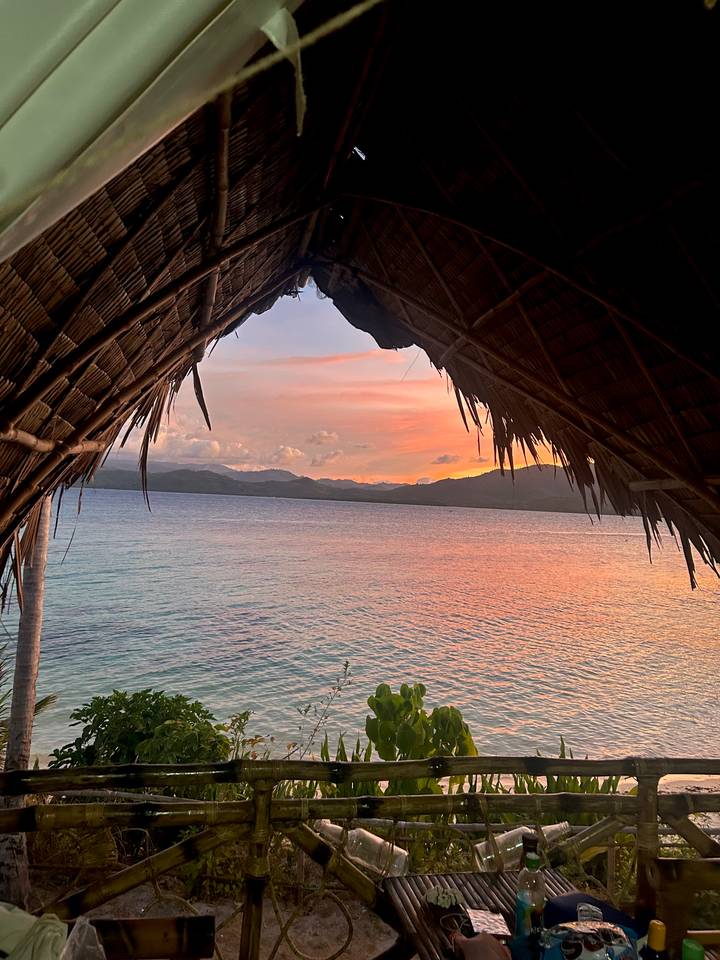 Idyllic sunset view of a calm turquoise sea framed by the thatched roof of a seaside hut.