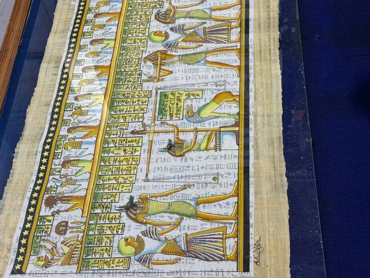Colourful papyrus artwork depicting ancient Egyptian gods and hieroglyphs on a royal blue background.