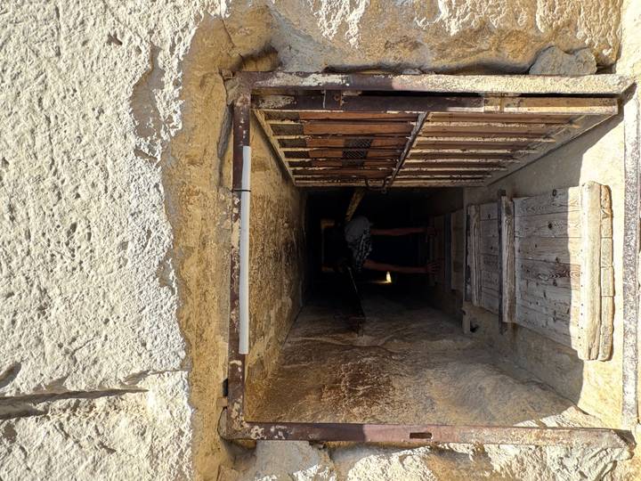 Visitor crouching to enter a narrow ancient stone passageway inside a pyramid.