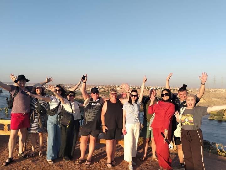Cheerful tour group raising their arms at a riverside viewpoint under clear blue skies