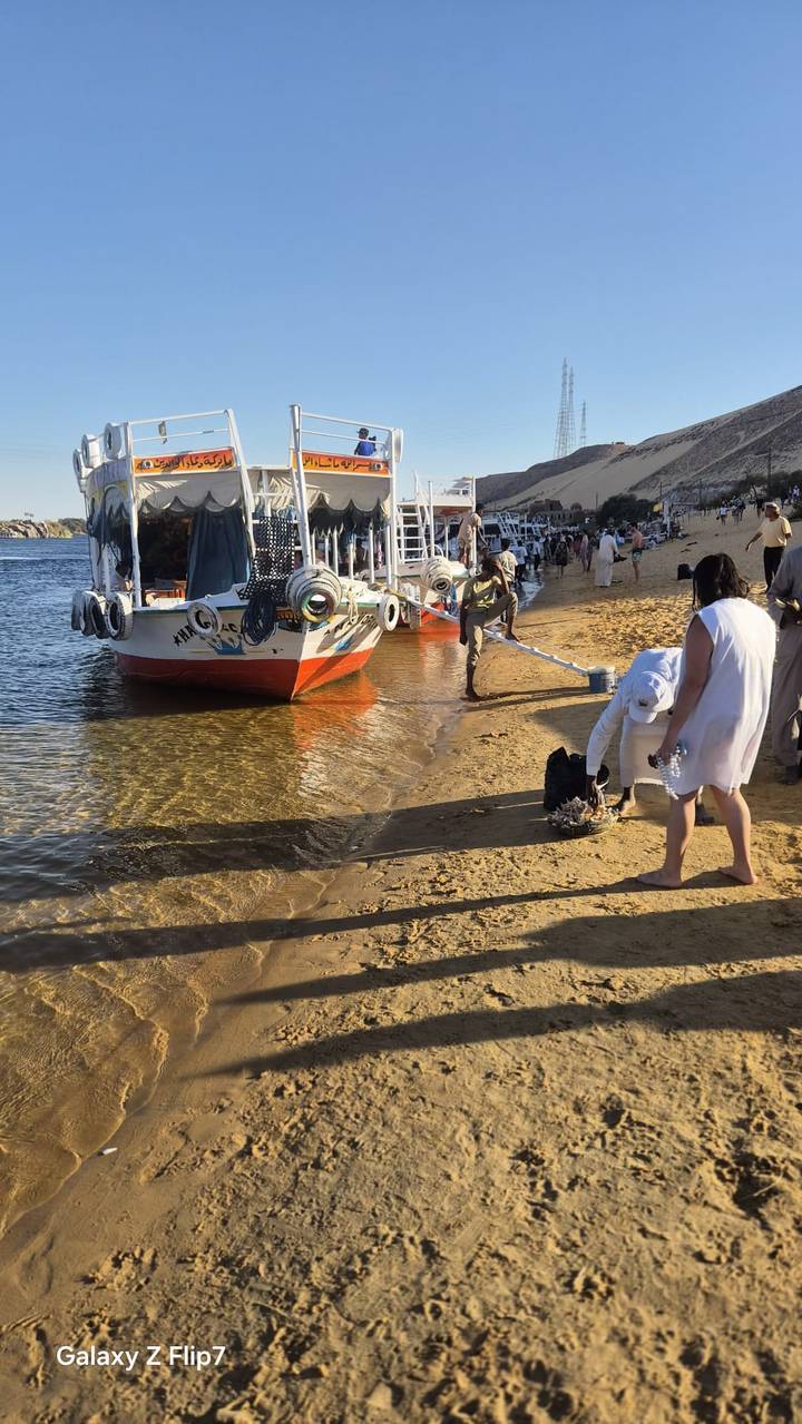 Small group boarding a white motorboat from a sandy riverbank with clear water