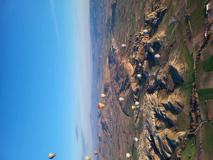Sweeping aerial view of Cappadocian valleys dotted with colourful hot-air balloons at sunrise.