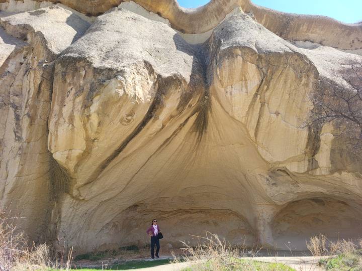 Large eroded rock face with cave-like recesses in Cappadocia, a traveller standing below for scale.