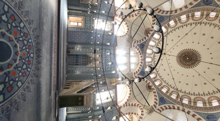 Intricately tiled interior of an Ottoman mosque with domed ceiling and patterned carpet lit by soft light.