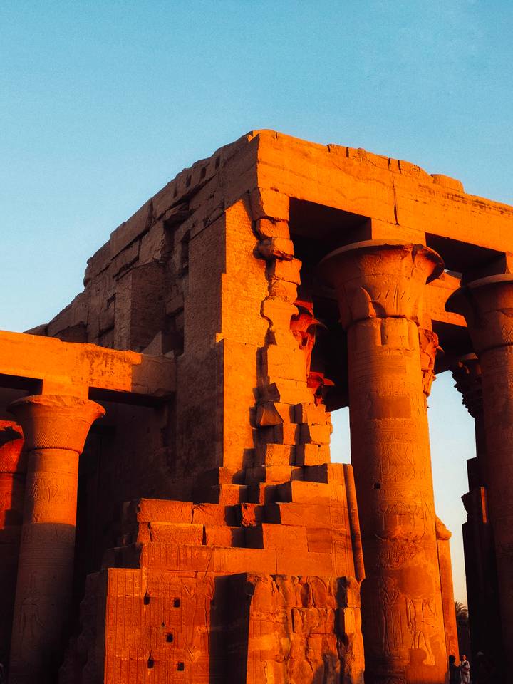 Close-up of ancient Egyptian columns bathed in warm orange late-day sunlight highlighting carved hieroglyphics.