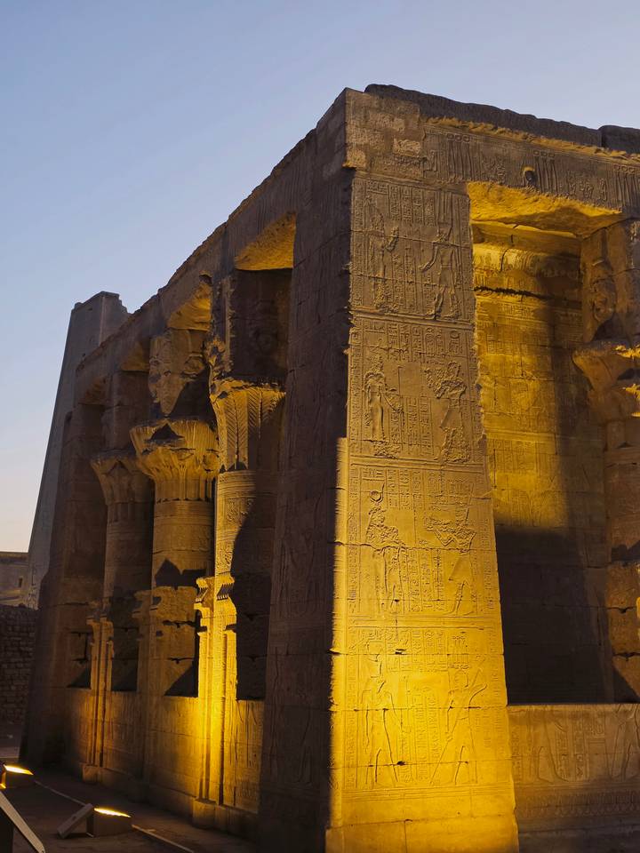 Night-lit Egyptian temple column covered in hieroglyphics glowing golden against surrounding dark stone walls.