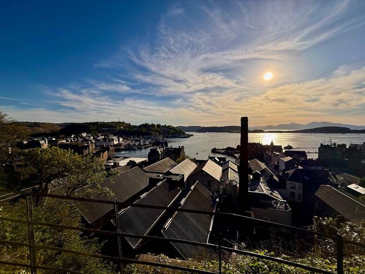 Sunset over a coastal Scottish town and harbour with rooftops in silhouette and shimmering water.