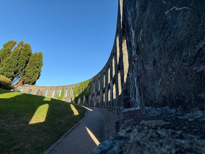 Upward perspective of the curved stone arches of McCaig’s Tower against a clear blue sky.