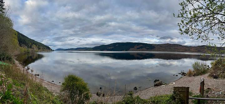 Serene panorama of a mirror-still loch reflecting rolling hills and a cloudy sky.