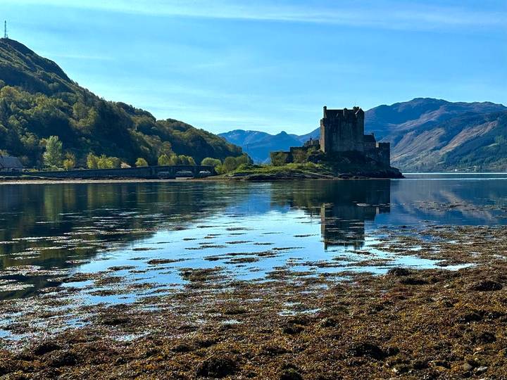 Iconic Eilean Donan Castle silhouetted against mountains and perfectly reflected in calm tidal waters.