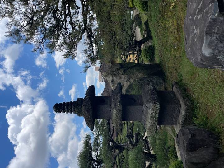 Stone pagoda and manicured pines in a traditional Japanese garden under blue skies with clouds.
