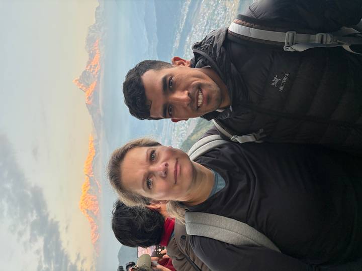 Two trekkers posing with snow-capped Himalayan peaks glowing in warm light behind them.