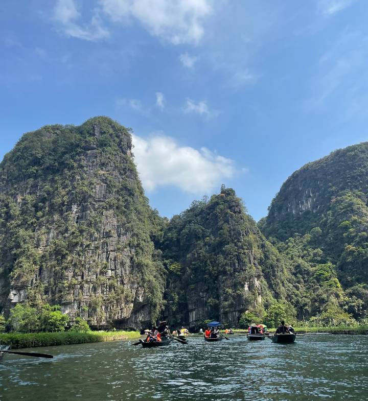 Steep green karst peaks rise against a blue sky dotted with soft white clouds.