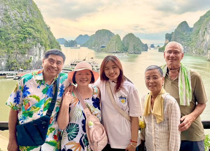Family poses with smiling faces on a cruise deck overlooking the limestone towers of Halong Bay.