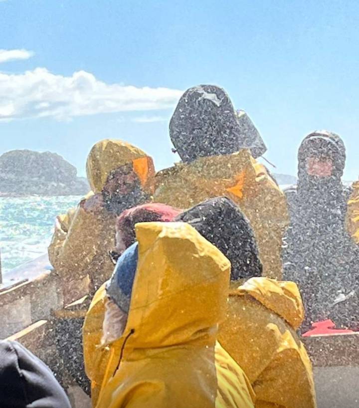 Passengers in yellow waterproof suits are doused by sea spray during a fast boat ride on rough waters.