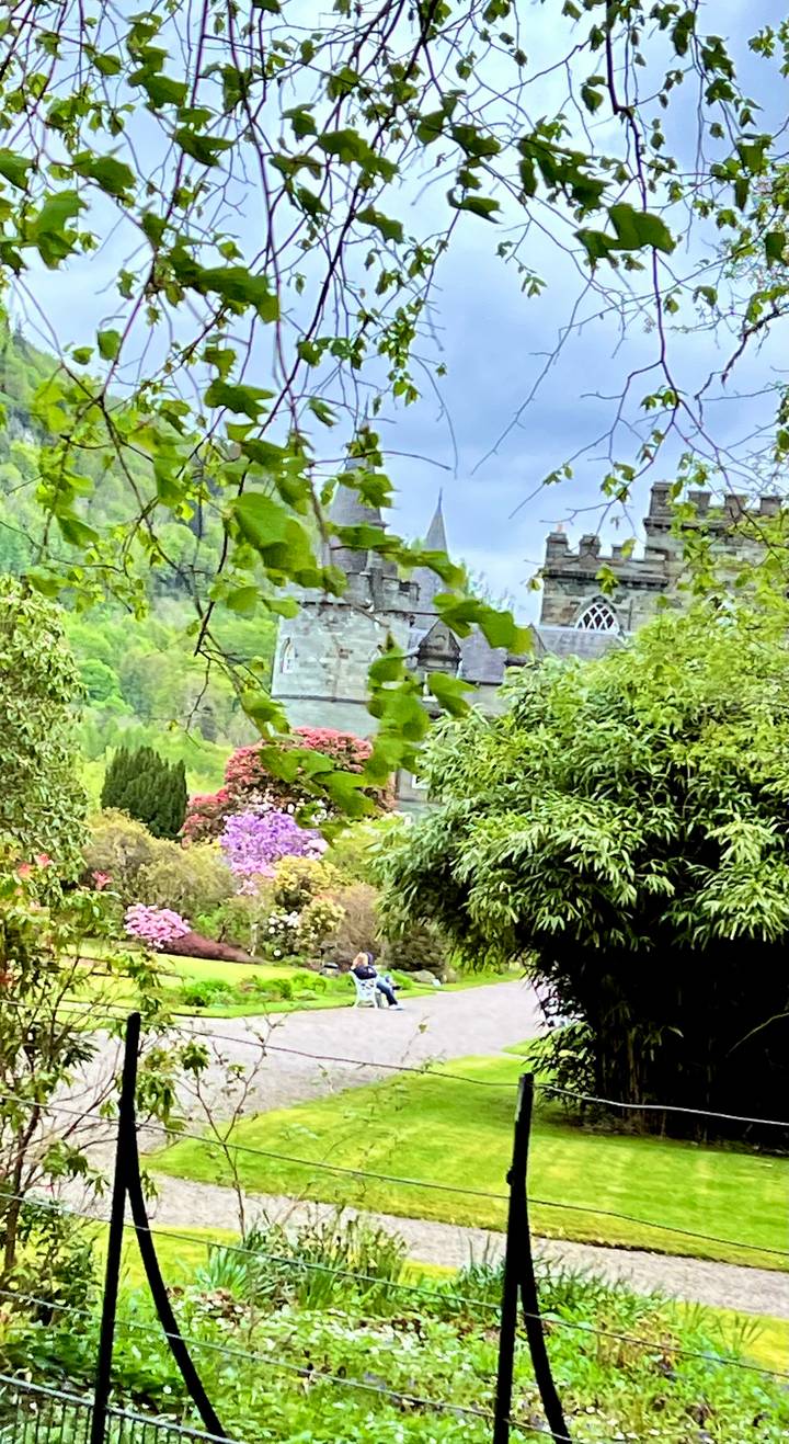 Stone castle partially hidden behind lush spring foliage and colourful rhododendrons in the Scottish Highlands.