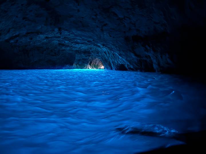 Glowing blue water fills a dark sea cave with light streaming from a distant entrance.