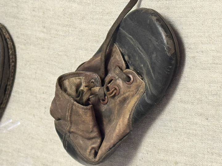 A worn, child-sized leather shoe displayed on a neutral fabric surface in a museum exhibit.