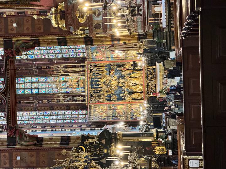 Ornate gilded altarpiece and vivid stained-glass windows inside a grand gothic basilica.