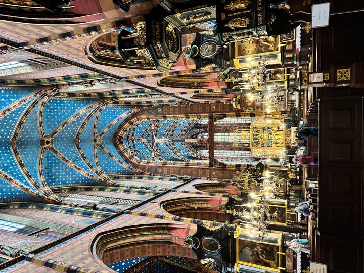 Central nave of a gothic basilica with blue starry ceiling, chandeliers and golden altar.