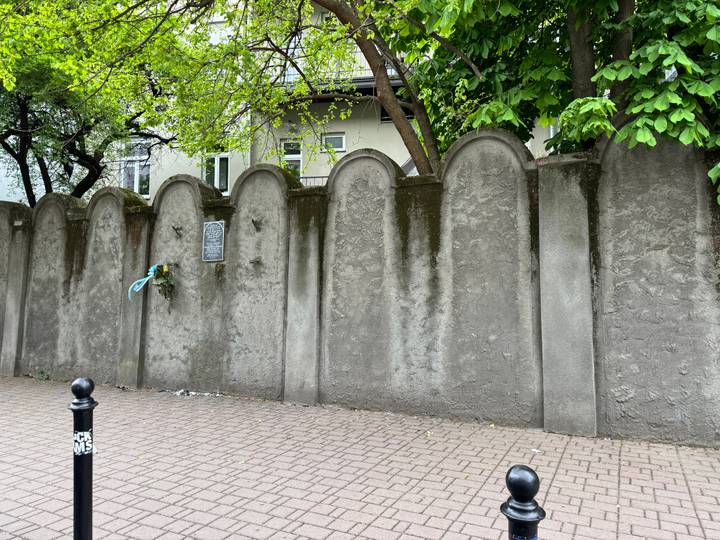 Grey concrete wall with rounded tombstone-shaped panels and a small memorial plaque beneath trees.