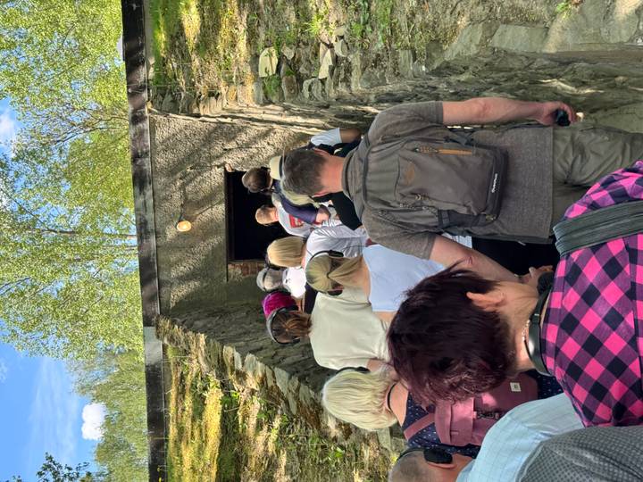 Line of tourists wearing headsets walking down a stone passage toward an underground doorway.