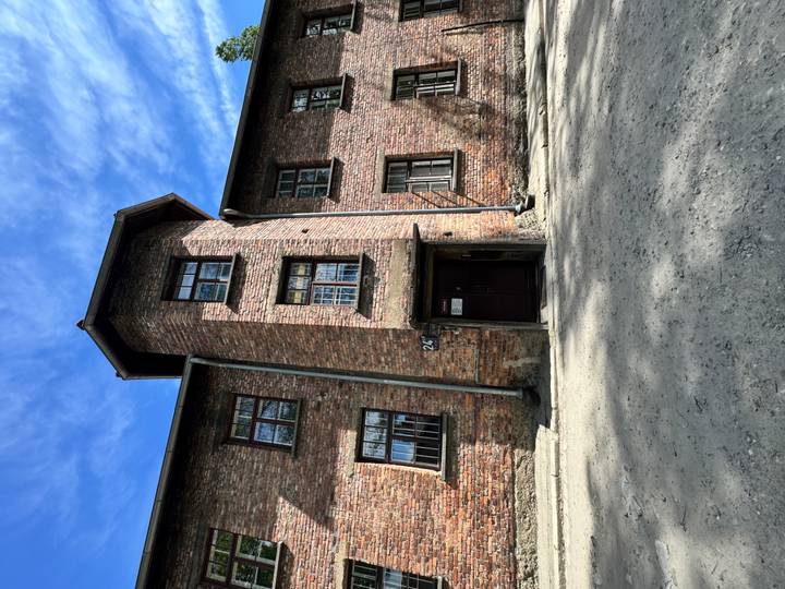 Red-brick barrack building with tall central tower and dark entrance door under blue sky.