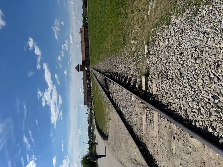 Railway tracks leading through the brick gatehouse of Birkenau under a bright blue sky.