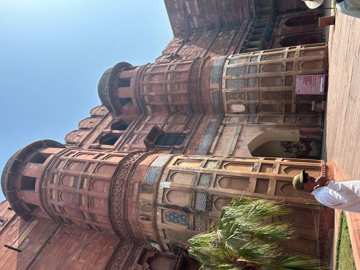 Massive red sandstone gateway tower of Agra Fort with a visitor standing in the sunlit forecourt.