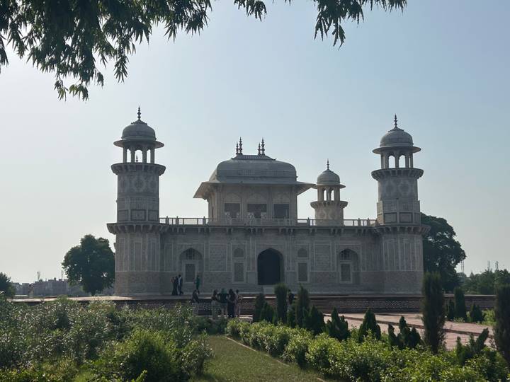 Silhouetted marble tomb of Itimad-ud-Daulah with small groups of visitors against a bright sky.