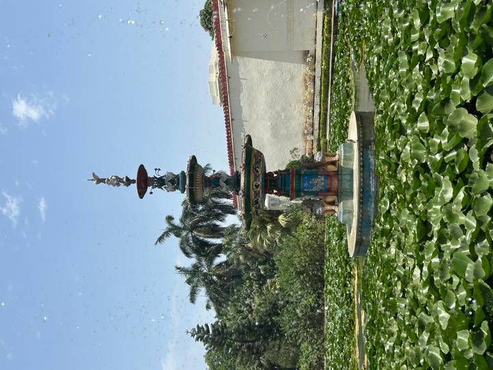 Colorful tiered fountain surrounded by lily pads in a sunny courtyard with palm trees.