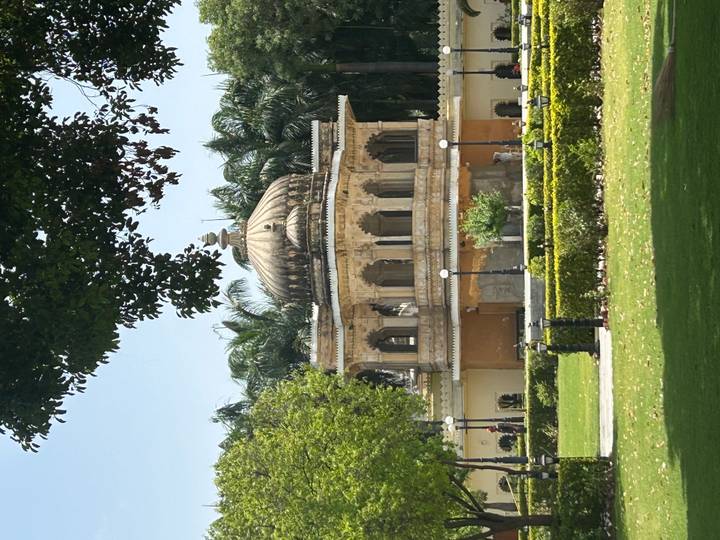 Ornate pavilion set within a manicured garden under bright sunshine.
