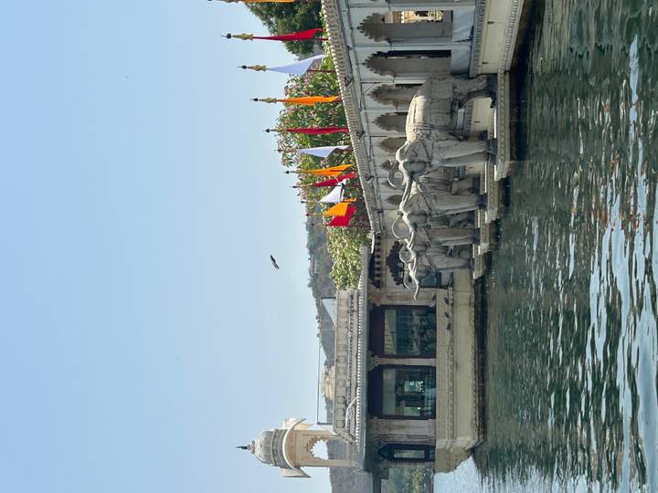 Row of carved elephant statues along the lake edge with colorful flags fluttering nearby.