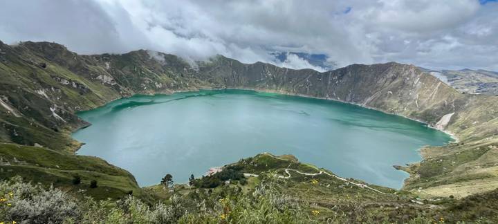 Panoramic view of the emerald Quilotoa crater lake ringed by dramatic cliffs beneath a cloudy sky.