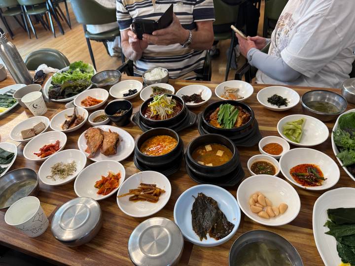 Traditional Korean meal spread of numerous banchan dishes on a wooden table with diners